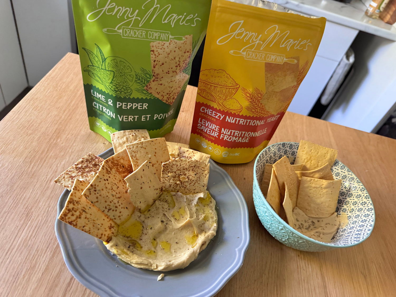 Bowl of lentil hummus with a bag of Lime & Pepper crackers and Cheezy Crackers